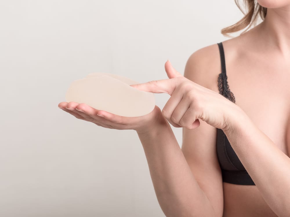 Woman holding a breast implant and considering how her implants will age over time.